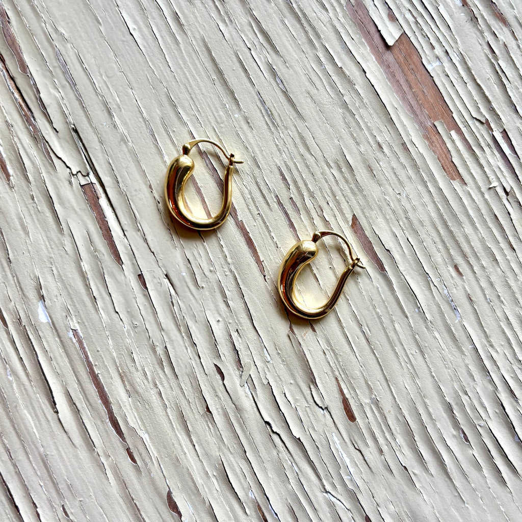 Gold hoop earrings on a textured wooden surface-iris 1956 jewelry