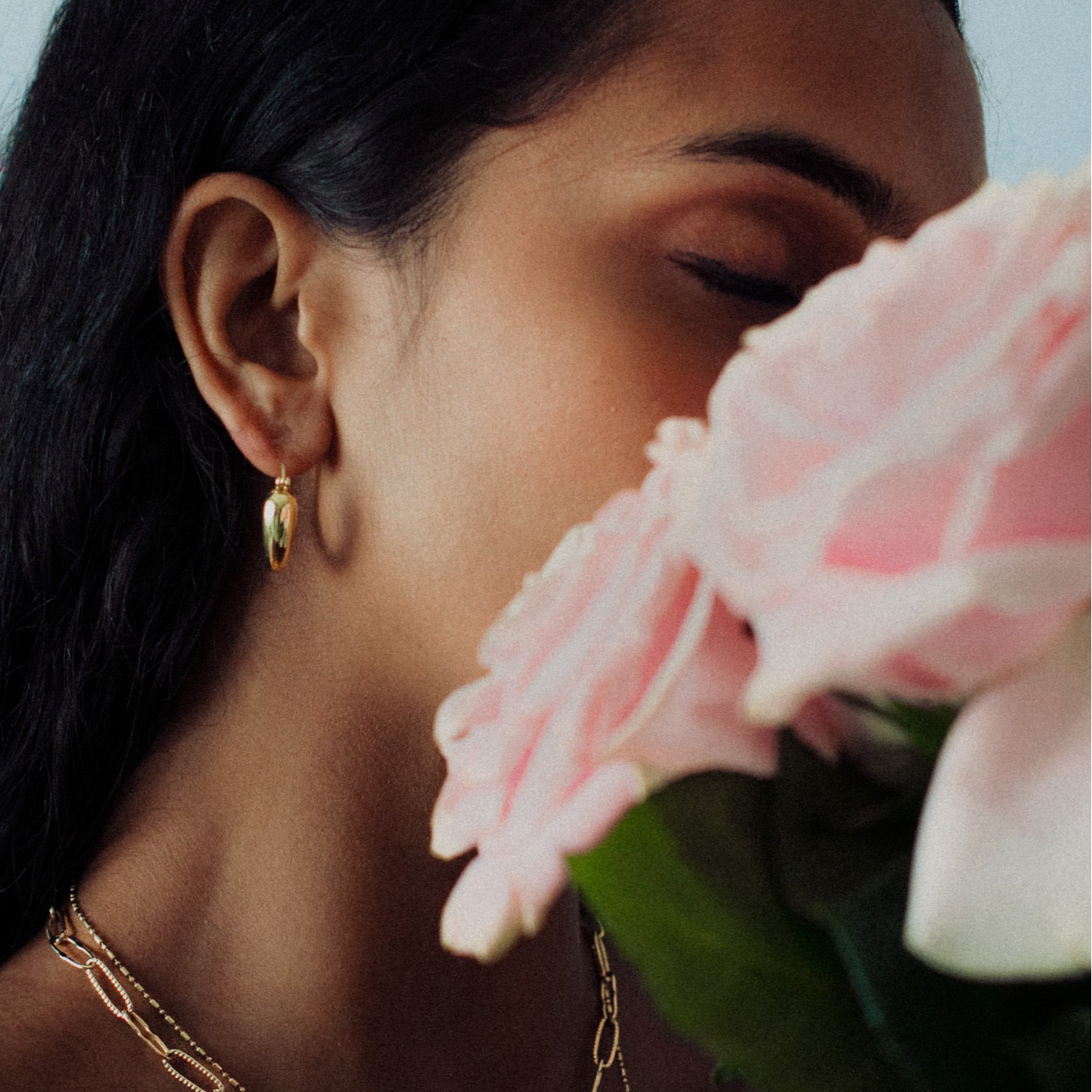 Woman wearing gold earrings and a necklace with pink flowers in the foreground